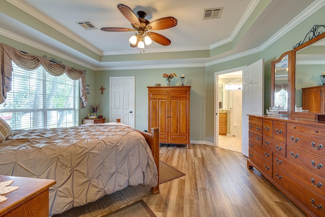 bedroom with ensuite bath, ceiling fan, a tray ceiling, ornamental molding, and light wood-type flooring