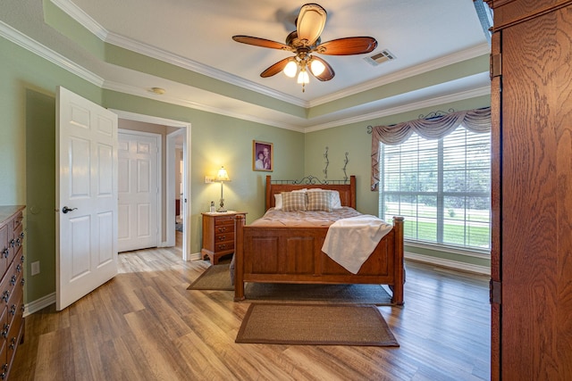 bedroom with crown molding, ceiling fan, light wood-type flooring, and a tray ceiling