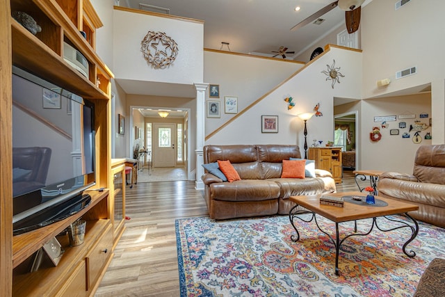 living room with a towering ceiling, light hardwood / wood-style flooring, decorative columns, and ceiling fan