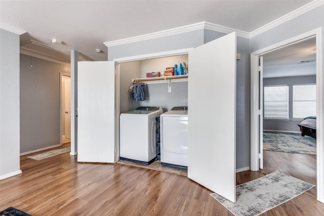 clothes washing area featuring light hardwood / wood-style flooring, ornamental molding, and washing machine and clothes dryer