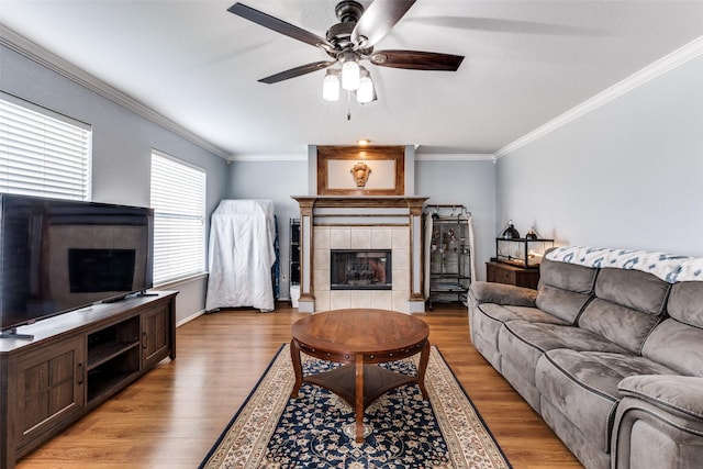 living room featuring a tile fireplace, light hardwood / wood-style floors, ceiling fan, and ornamental molding