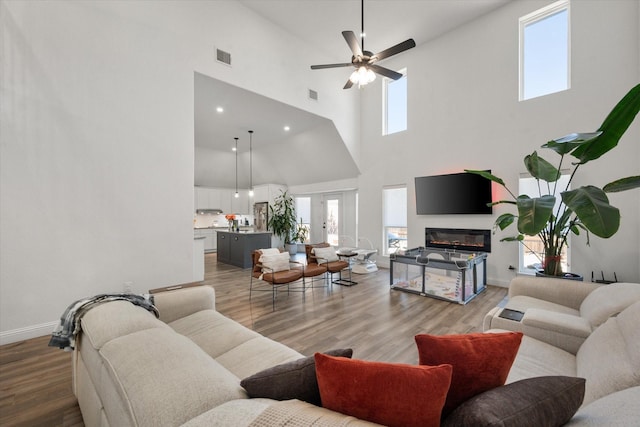 living room with ceiling fan, wood-type flooring, a towering ceiling, and a wealth of natural light