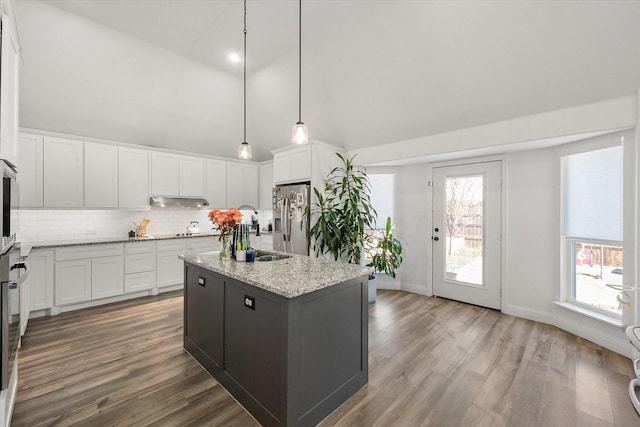 kitchen featuring white cabinets, hanging light fixtures, stainless steel fridge with ice dispenser, light stone countertops, and a center island with sink