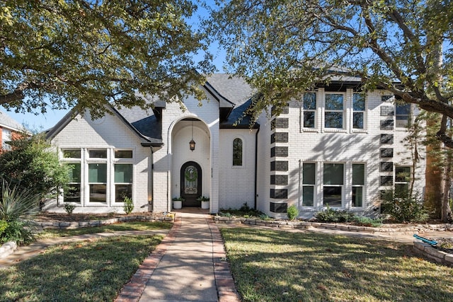 french provincial home with brick siding, a front lawn, and roof with shingles