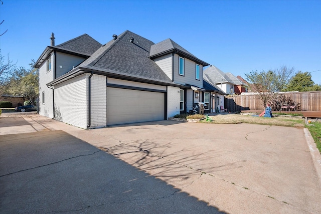 exterior space featuring brick siding, roof with shingles, fence, a garage, and driveway