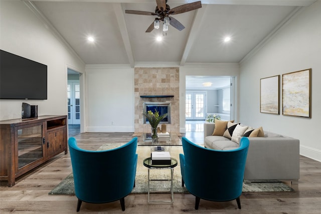 living room with vaulted ceiling with beams, ceiling fan, ornamental molding, wood-type flooring, and a tiled fireplace