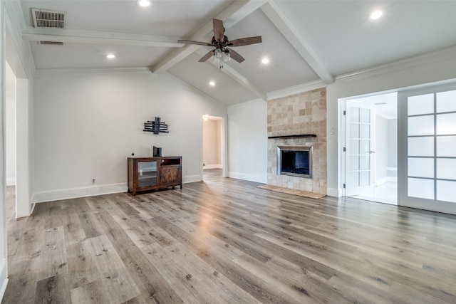 unfurnished living room with a tile fireplace, ceiling fan, lofted ceiling with beams, crown molding, and light hardwood / wood-style floors