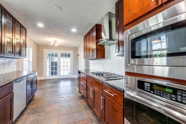 kitchen with appliances with stainless steel finishes, backsplash, french doors, wall chimney exhaust hood, and a textured ceiling