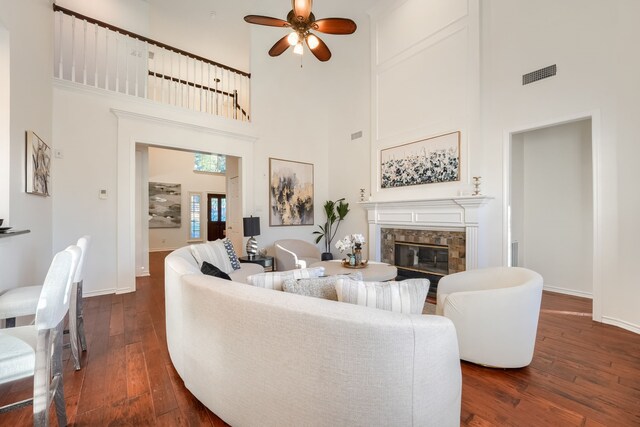 living room with a tiled fireplace, ceiling fan, dark hardwood / wood-style floors, and a high ceiling