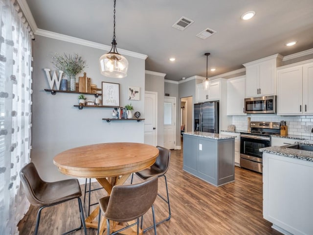 kitchen featuring decorative backsplash, white cabinetry, stainless steel appliances, and hanging light fixtures