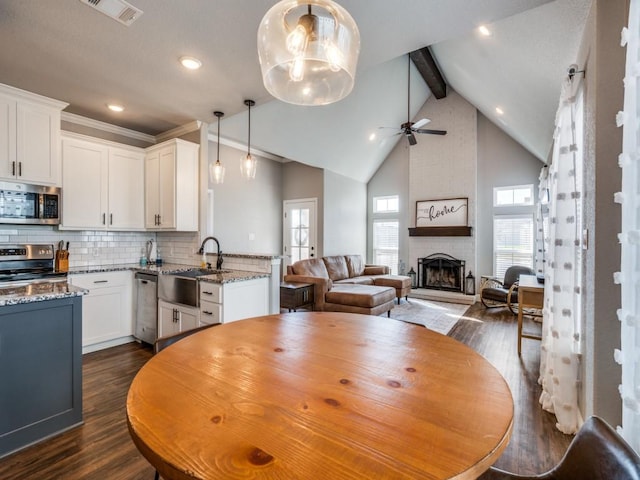 dining space with a brick fireplace, ceiling fan, sink, beam ceiling, and high vaulted ceiling