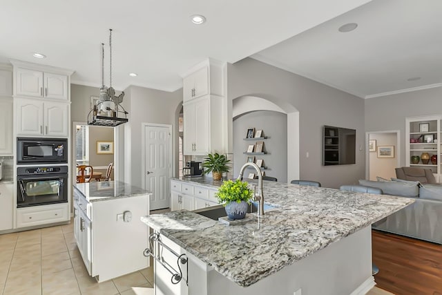 kitchen featuring a center island with sink, black appliances, sink, light tile patterned flooring, and light stone counters