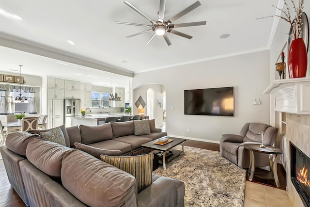 living room with ceiling fan, sink, crown molding, and a tile fireplace