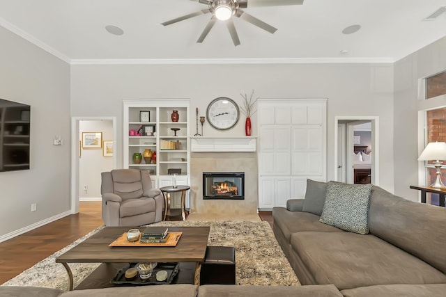 living room featuring ornamental molding, built in shelves, ceiling fan, a tile fireplace, and hardwood / wood-style floors