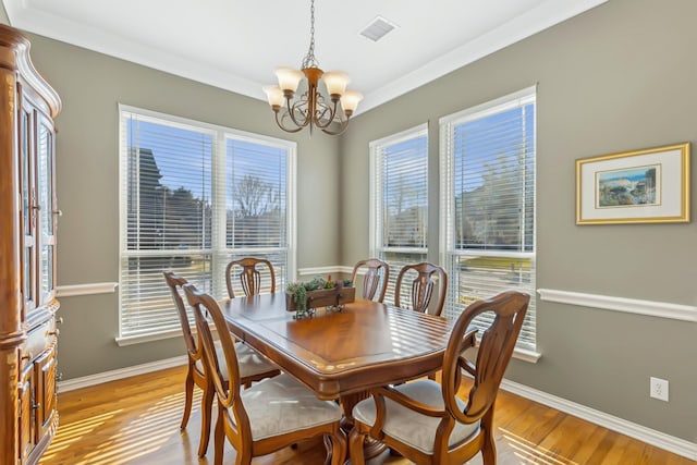 dining space with light wood-type flooring, ornamental molding, and an inviting chandelier