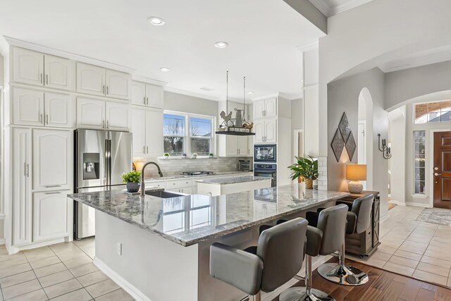 kitchen featuring sink, light tile patterned floors, appliances with stainless steel finishes, decorative light fixtures, and white cabinetry