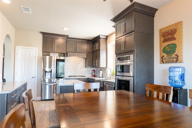 kitchen with dark brown cabinetry, appliances with stainless steel finishes, light stone countertops, light hardwood / wood-style floors, and backsplash