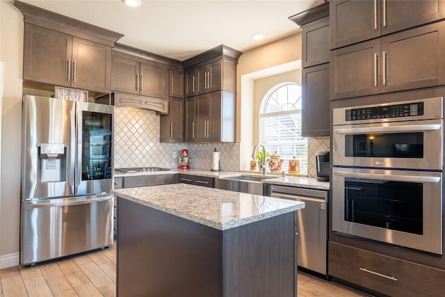 kitchen featuring a center island, sink, light hardwood / wood-style flooring, light stone countertops, and stainless steel appliances