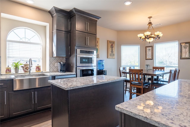 kitchen featuring pendant lighting, an inviting chandelier, a kitchen island, light stone counters, and stainless steel double oven