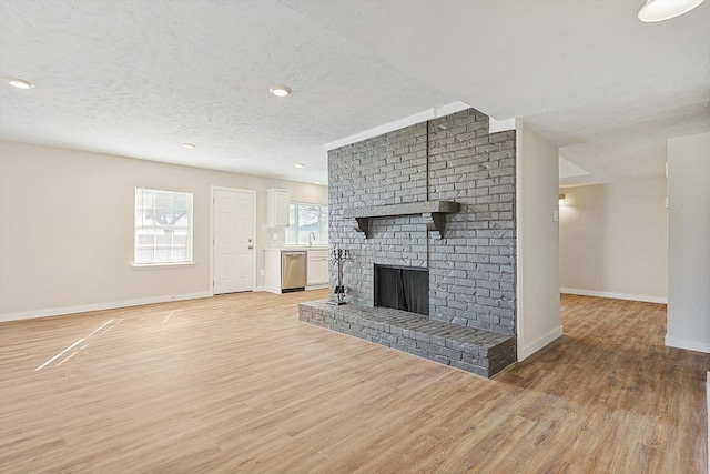 unfurnished living room with a fireplace, a textured ceiling, light hardwood / wood-style flooring, and sink