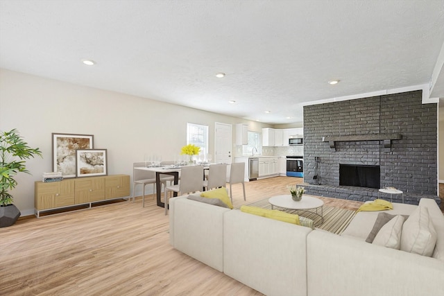 living room featuring a fireplace, sink, light hardwood / wood-style flooring, and a textured ceiling