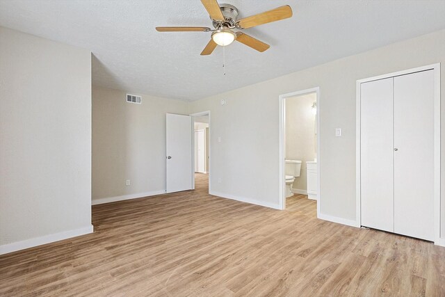 unfurnished bedroom featuring ceiling fan, ensuite bathroom, light hardwood / wood-style floors, a textured ceiling, and a closet