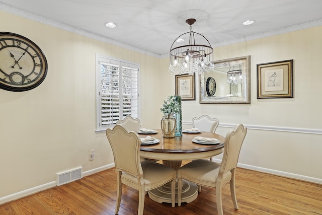 dining room with light hardwood / wood-style floors, crown molding, and an inviting chandelier