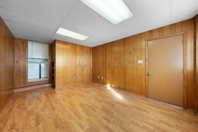 spare room with a paneled ceiling, wood walls, light wood-type flooring, and independent washer and dryer