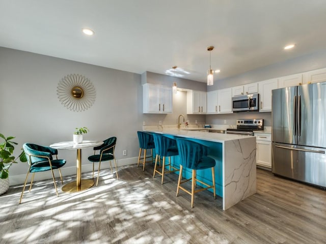 kitchen featuring white cabinets, appliances with stainless steel finishes, a kitchen bar, and pendant lighting