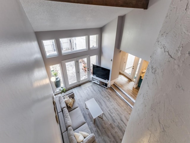 unfurnished living room featuring a towering ceiling, a textured ceiling, and light hardwood / wood-style flooring