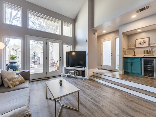 living room featuring wine cooler, a towering ceiling, light hardwood / wood-style floors, and wet bar