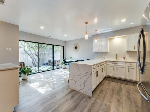 kitchen with stainless steel refrigerator, decorative light fixtures, white cabinets, light stone counters, and kitchen peninsula