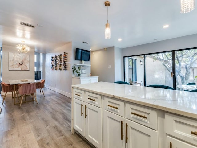 kitchen featuring white cabinetry, light stone counters, light hardwood / wood-style floors, and hanging light fixtures