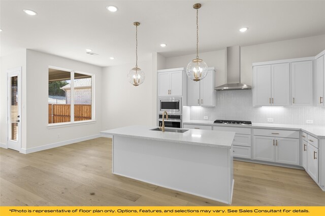 kitchen featuring sink, wall chimney exhaust hood, stainless steel appliances, an island with sink, and white cabinets