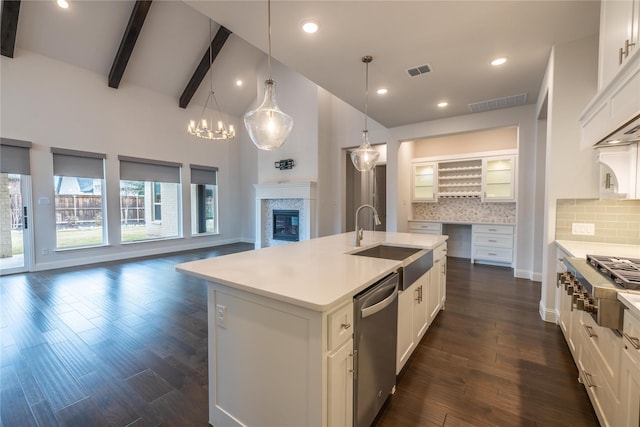 kitchen with stainless steel appliances, a center island with sink, backsplash, beamed ceiling, and sink