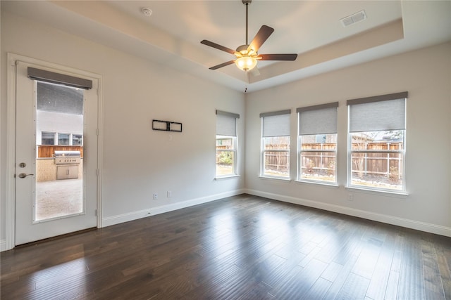 empty room featuring a raised ceiling, ceiling fan, and dark wood-type flooring