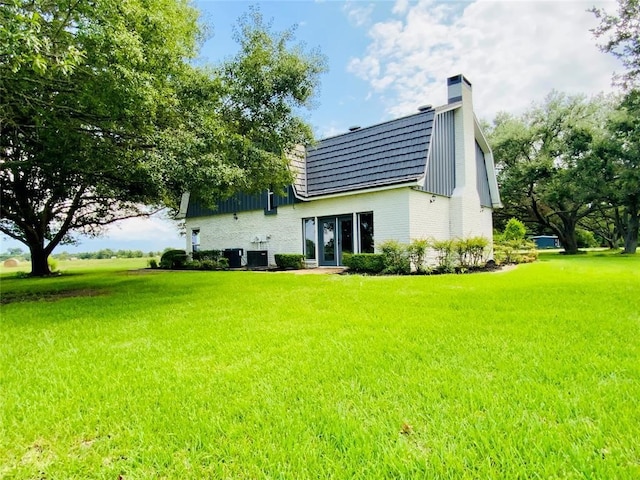 rear view of property with central AC unit and a yard