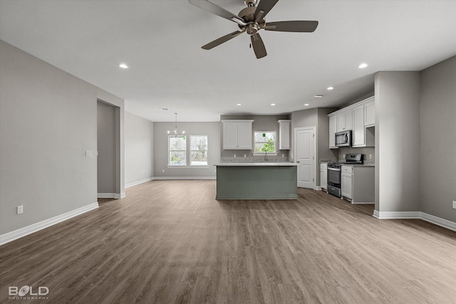 kitchen featuring open floor plan, stainless steel appliances, wood finished floors, and baseboards