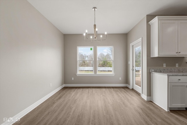 unfurnished dining area with a chandelier, light wood-type flooring, and baseboards