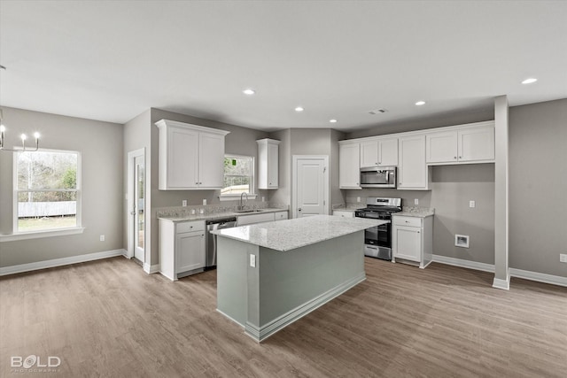 kitchen featuring white cabinets, appliances with stainless steel finishes, a center island, light wood-style floors, and a sink