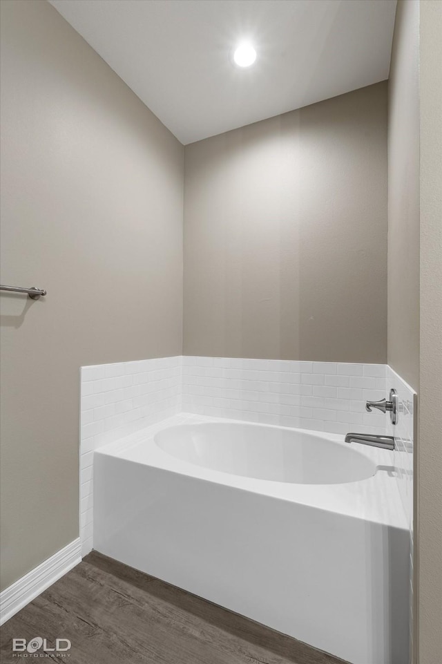 bathroom featuring wood finished floors, a garden tub, and baseboards