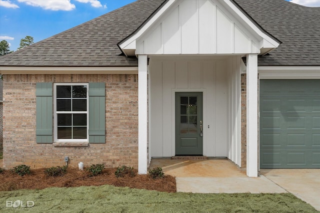 property entrance with a shingled roof, brick siding, board and batten siding, and an attached garage