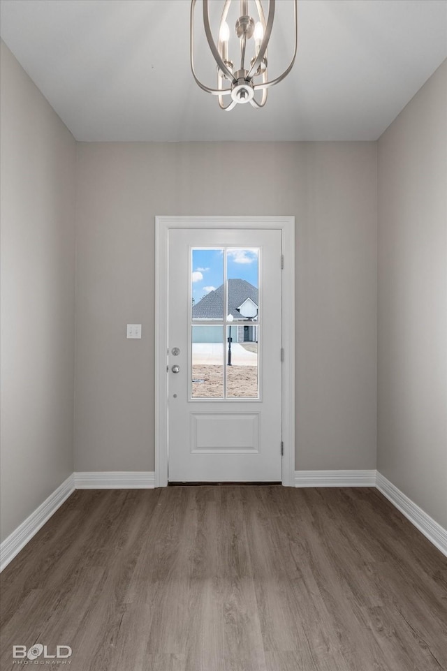 doorway with a chandelier, baseboards, and wood finished floors