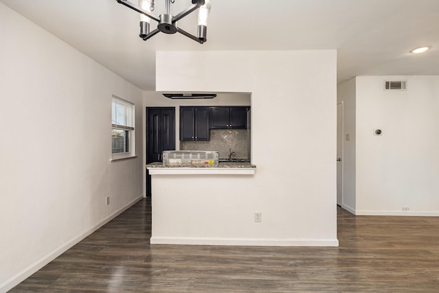 kitchen with dark hardwood / wood-style flooring, tasteful backsplash, kitchen peninsula, a chandelier, and light stone counters