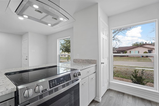 kitchen featuring light stone countertops, light wood-type flooring, stainless steel range, island range hood, and white cabinets