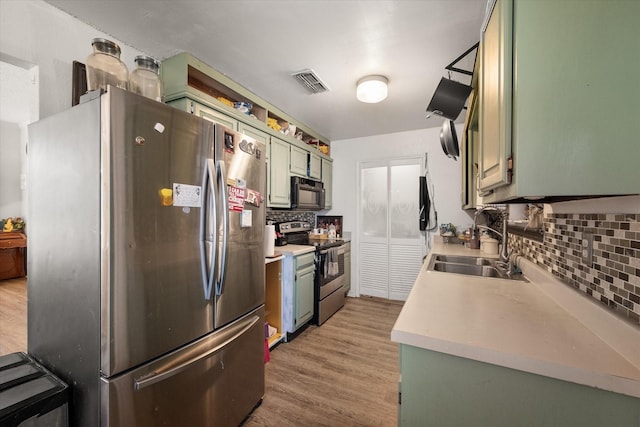 kitchen featuring tasteful backsplash, stainless steel appliances, sink, light hardwood / wood-style floors, and green cabinets