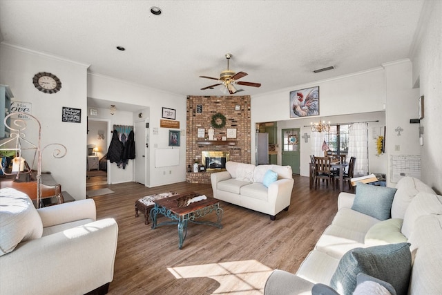 living room featuring ceiling fan with notable chandelier, a brick fireplace, ornamental molding, a textured ceiling, and wood-type flooring