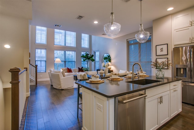 kitchen featuring white cabinetry, sink, stainless steel appliances, decorative light fixtures, and a center island with sink