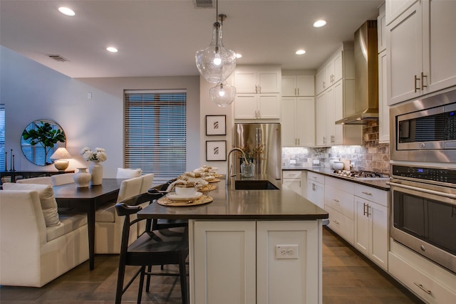 kitchen featuring sink, wall chimney exhaust hood, an island with sink, pendant lighting, and appliances with stainless steel finishes