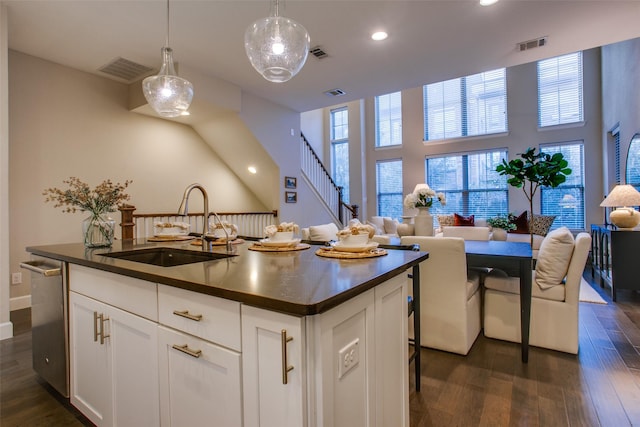 kitchen featuring dark wood-type flooring, sink, decorative light fixtures, a center island with sink, and white cabinets